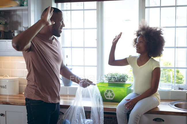 Fille afro-américaine et son père triant le recyclage ensemble dans la cuisine. rester à la maison en isolement personnel pendant le confinement en quarantaine. — Photo de stock