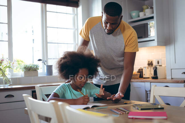 Chica afroamericana haciendo deberes con su padre. permanecer en casa en aislamiento durante el bloqueo de cuarentena. - foto de stock