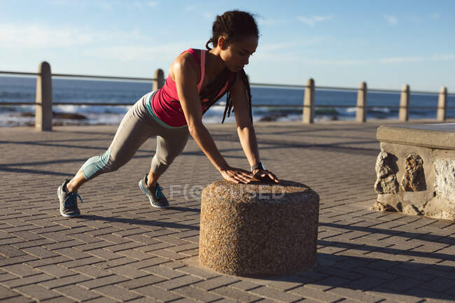 Eine Afroamerikanerin konzentriert sich beim Sport auf einer Strandpromenade. Fitness und gesunder Lebensstil im Freien. — Stockfoto