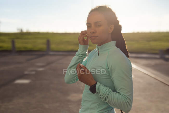 Mujer afroamericana concentrada, usando ropa deportiva haciendo ejercicio en el parque poniendo auriculares. Fitness estilo de vida saludable al aire libre. - foto de stock