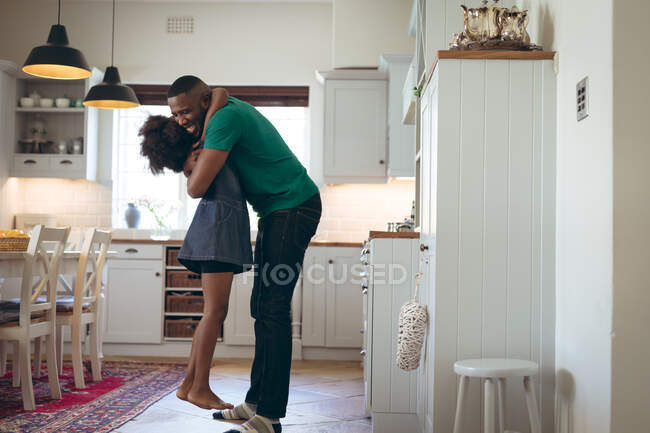 Chica afroamericana y su padre abrazándose en la cocina. permanecer en casa en aislamiento durante el bloqueo de cuarentena. - foto de stock