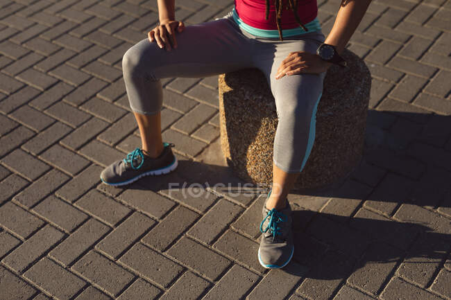 Midsection of woman taking break in exercise on a promenade by the sea, sitting. Fitness healthy outdoor lifestyle. — Stock Photo