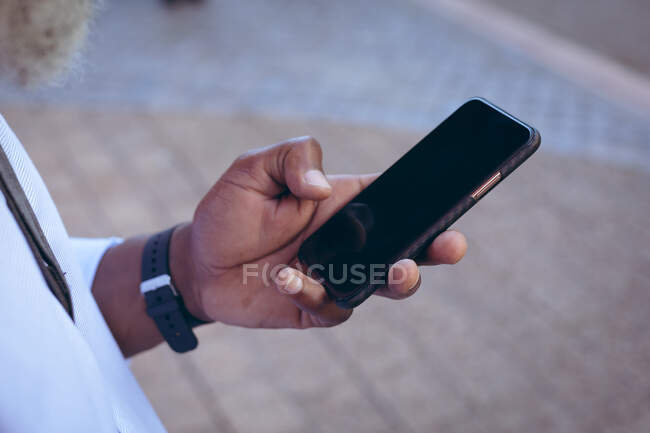 Sección media del hombre de pie en la calle usando un teléfono inteligente. nómada digital en la ciudad. - foto de stock