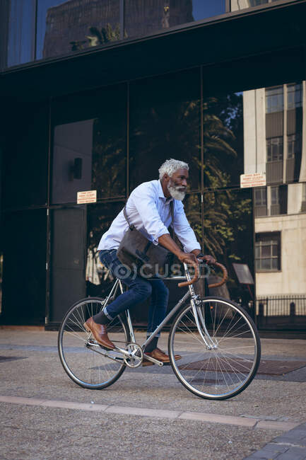 Африканський старший американець їде на велосипеді на вулиці повз двері. Цифровий кочівник і все в місті. — стокове фото