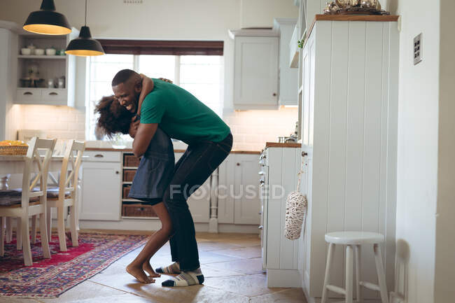 Africaine américaine fille et son père embrasser dans la cuisine. rester à la maison en isolement personnel pendant le confinement en quarantaine. — Photo de stock