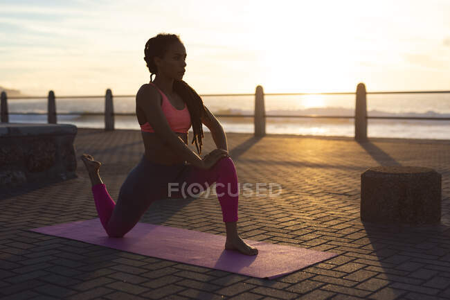 Femme afro-américaine faisant du yoga sur la promenade au bord de la mer. fitness mode de vie sain en plein air. — Photo de stock