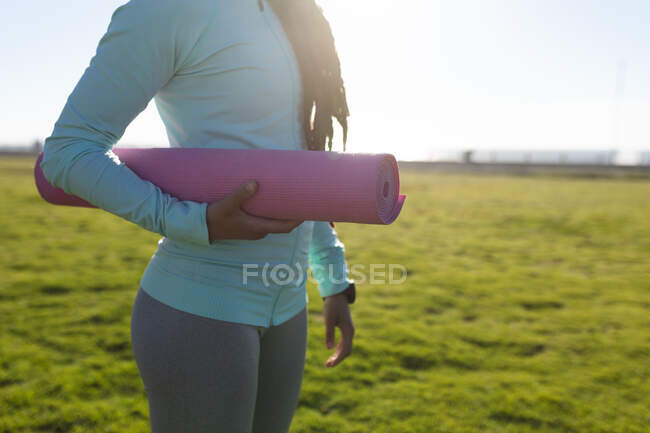 Midsection da mulher que exercita-se em um parque que carrega um tapete do ioga. Fitness estilo de vida ao ar livre saudável. — Fotografia de Stock
