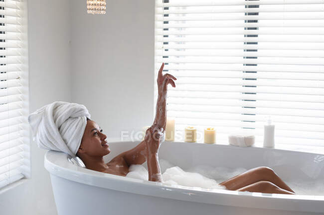 African american woman bathing in bathtub at bathroom. staying at home in self isolation in quarantine lockdown — Stock Photo