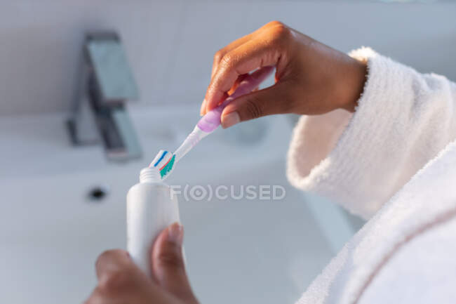 Sección media de poner pasta de dientes en el cepillo de dientes en el baño. permaneciendo en casa en aislamiento en cuarentena - foto de stock