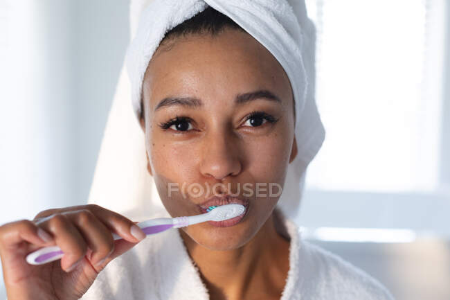 Portrait of african american woman brushing her teeth in bathroom. staying at home in self isolation in quarantine lockdown — Stock Photo
