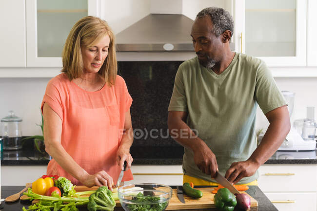 Diverse senior couple standing in kitchen and cooking dinner. staying at home in isolation during quarantine lockdown. — Stock Photo