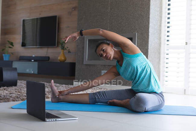 Африканська американка практикує йогу, дивлячись на екран ноутбука вдома. Залишатися вдома в ізоляції в карантині. — стокове фото