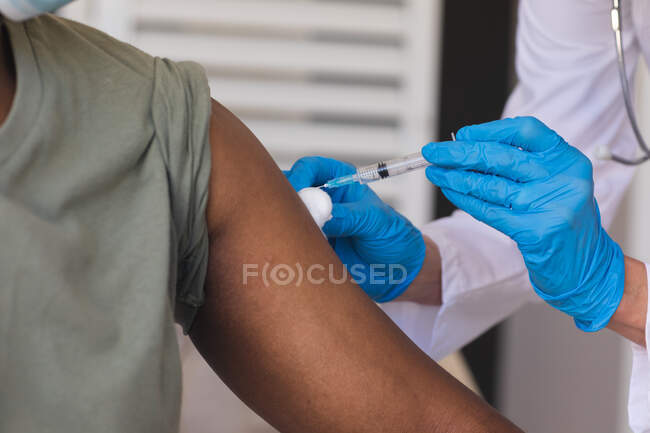 Старшая женщина-врач вакцинирует пожилого мужчину смешанной расы. медицинский работник на работе во время пандемии коронавируса. — стоковое фото