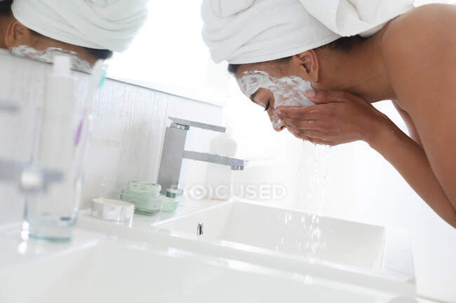 Uma afro-americana a lavar a máscara no lavatório da casa de banho. ficar em casa em auto-isolamento em quarentena — Fotografia de Stock