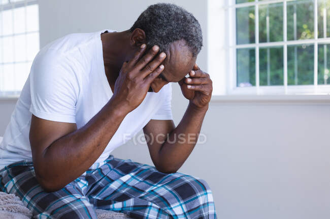 Змішана раса старший чоловік сидить на ліжку і тримає голову. перебування вдома в ізоляції під час карантину . — стокове фото