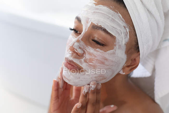 Close up de mulher afro-americana aplicando máscara facial no banheiro. ficar em casa em auto-isolamento em quarentena — Fotografia de Stock