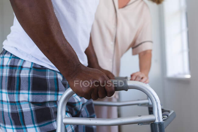 Mixed race senior man walking with crunches with caucasian senior woman helping. staying at home in isolation during quarantine lockdown. — Stock Photo