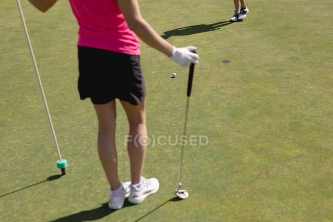 Donna che gioca a golf tenendo club e bandiera, mentre altri giocatori putt per il buco. sport hobby sano stile di vita all'aperto. — Foto stock
