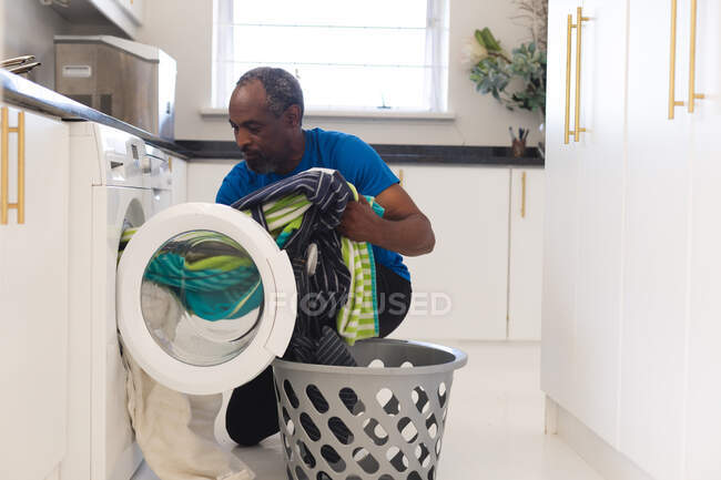 Старший смешанной расы загружает стиральную машину. оставаться дома в изоляции во время карантинной изоляции. — стоковое фото