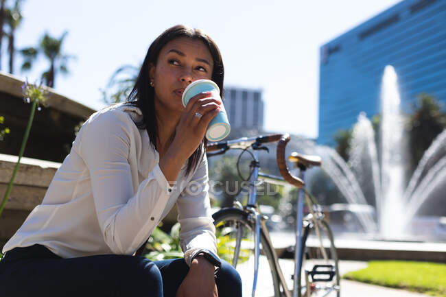 Mulher de raça mista sentada no parque bebendo café. mulher em movimento e sobre a cidade. — Fotografia de Stock