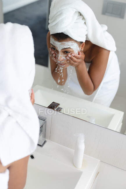 Mujer afroamericana lavándose la mascarilla en el lavabo del baño. permaneciendo en casa en aislamiento en cuarentena - foto de stock