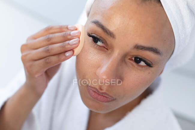 Закрийте афроамериканську жінку, що прибирає обличчя губкою у ванній кімнаті. Залишатися вдома в ізоляції в карантині. — стокове фото