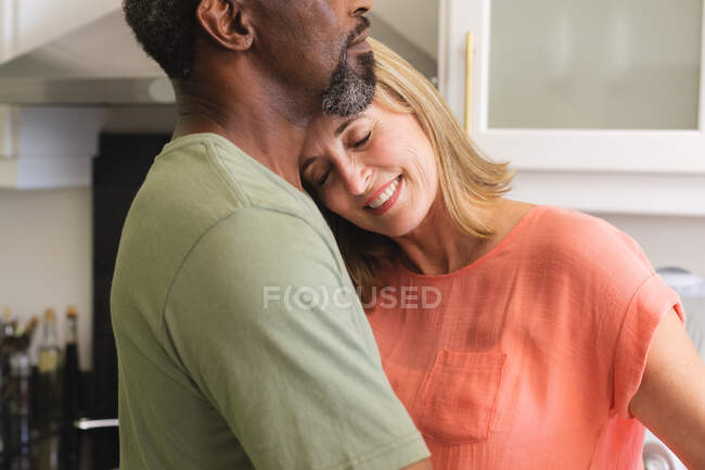 Casal sênior diverso dançando na cozinha e abraçando. ficar em casa em isolamento durante o confinamento de quarentena. — Fotografia de Stock