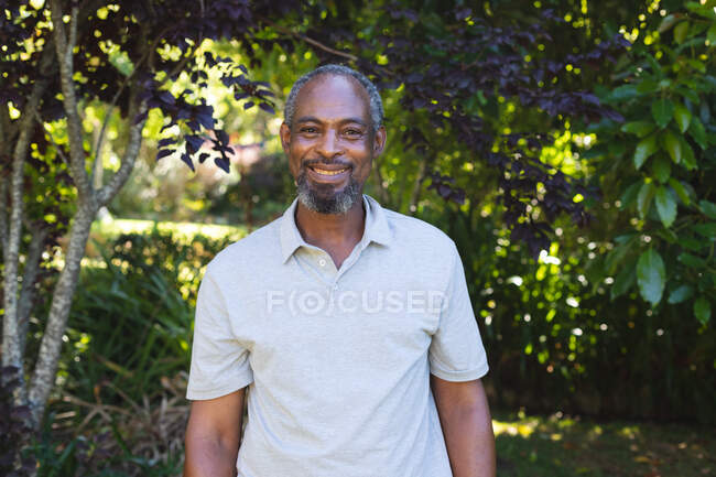 Porträt eines älteren Mannes mit gemischter Rasse im Garten, der in die Kamera blickt und lächelt. Isolationshaft während der Quarantäne. — Stockfoto