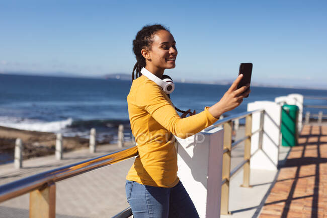 Lächelnde Afroamerikanerin beim Selfie mit dem Smartphone am Meer. digitaler Nomade unterwegs. — Stockfoto