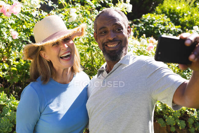 Diverse senior couple in garden taking selfie with smartphone. staying at home in isolation during quarantine lockdown. — Stock Photo