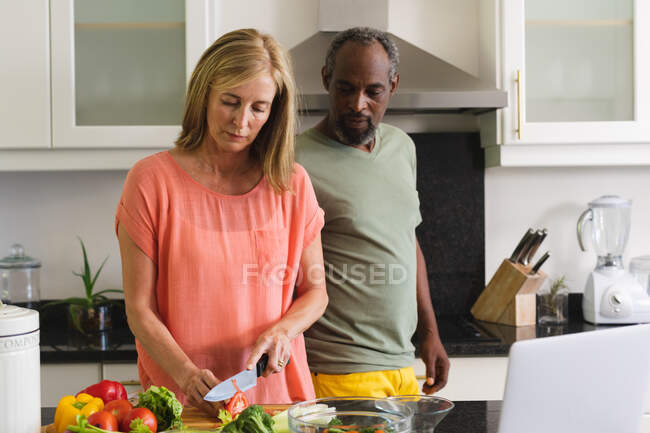 Разнообразная старшая пара, стоящая на кухне и готовящая ужин. оставаться дома в изоляции во время карантинной изоляции. — стоковое фото