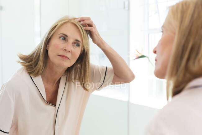 Caucasian senior woman standing in bathroom doing her hair. staying at home in isolation during quarantine lockdown. — Stock Photo
