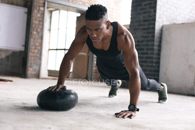 African american man exercising in warehouse doing push ups with medicine ball. healthy active urban lifestyle. — Stock Photo
