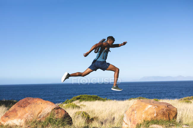 Homem afro-americano se exercitando ao ar livre pulando em uma montanha. treinamento de fitness e estilo de vida saudável ao ar livre. — Fotografia de Stock