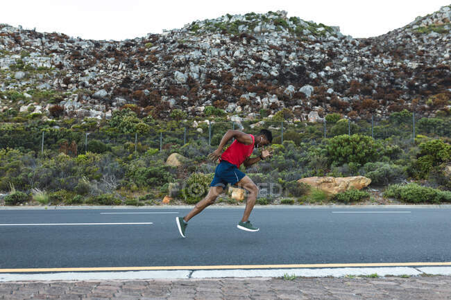 African american man exercising outdoors running on a coastal road. fitness training and healthy outdoor lifestyle. — Stock Photo