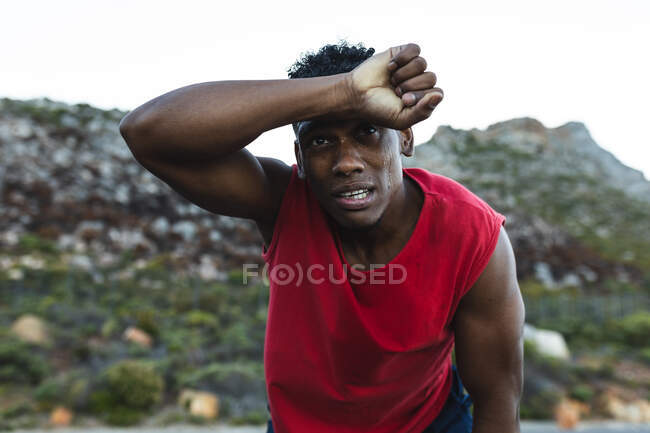 Ritratto di uomo afroamericano stanco in forma che si allena all'aperto su una strada costiera. allenamento fitness e stile di vita sano all'aperto. — Foto stock