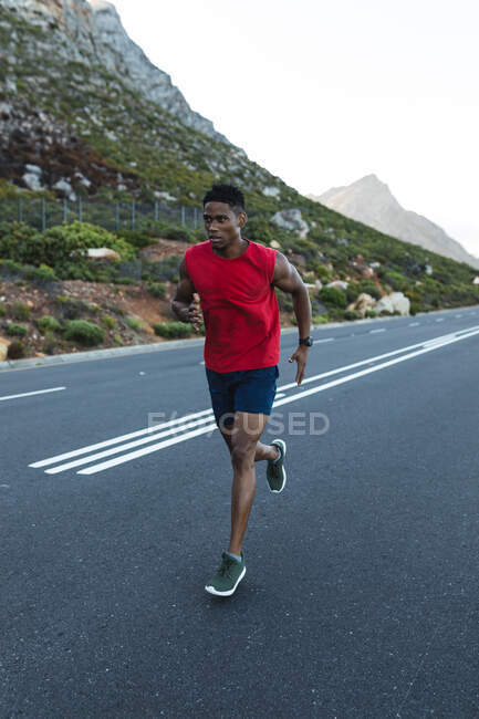 African american man exercising outdoors running on a coastal road. fitness training and healthy outdoor lifestyle. — Stock Photo