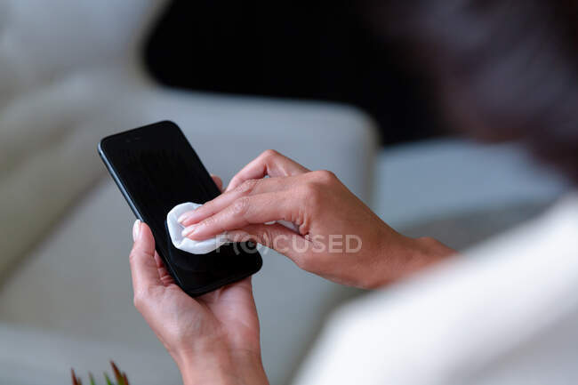 Midsection of businesswoman sitting disinfecting smartphone. business person at work in modern office during covid 19 coronavirus pandemic. — Stock Photo