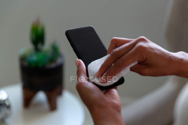 Midsection of mixed race businesswoman disinfecting smartphone. business person at work in modern office during covid 19 coronavirus pandemic. — Stock Photo