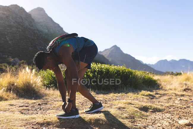 Африканский американец тренируется на открытом воздухе, завязывая ботинки на горе. фитнес-тренировки и здоровый образ жизни. — стоковое фото