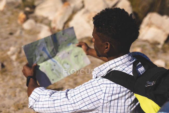 Uomo afroamericano che si allena all'aperto leggendo la mappa su una montagna. allenamento fitness e stile di vita sano all'aperto. — Foto stock