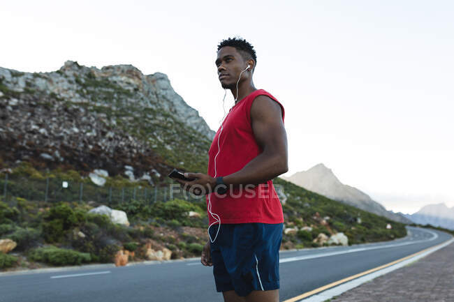 Afrikanischer Mann beim Training im Freien, stehend auf einer Küstenstraße. Fitnesstraining und gesunder Lebensstil im Freien. — Stockfoto