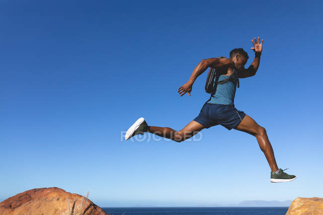Homem afro-americano se exercitando ao ar livre pulando em uma montanha. treinamento de fitness e estilo de vida saudável ao ar livre. — Fotografia de Stock
