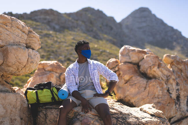 Portrait eines fitten afrikanisch-amerikanischen Mannes im Freien auf einem Felsen auf einem Berg sitzend. Fitnesstraining und gesunder Lebensstil im Freien. — Stockfoto