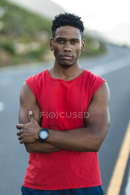 Retrato del hombre afroamericano en forma ejercitando al aire libre en una carretera costera a cámara. entrenamiento de fitness y estilo de vida saludable al aire libre. - foto de stock