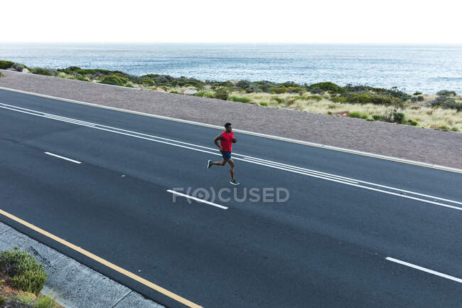 Africano americano exercitando ao ar livre correndo em uma estrada costeira. treinamento de fitness e estilo de vida saudável ao ar livre. — Fotografia de Stock