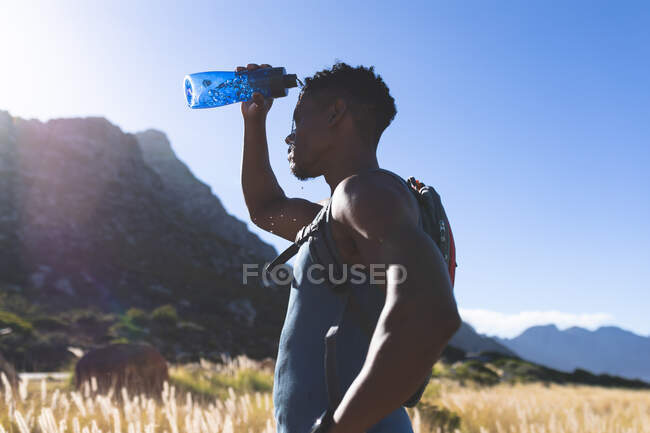 Afroamerikanischer Mann beim Sport im Freien, der Wasser auf einen Berg gießt. Fitnesstraining und gesunder Lebensstil im Freien. — Stockfoto