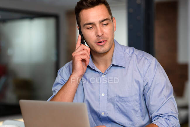 Портрет випадкового кавказького бізнесмена, який розмовляє по смартфону, сидячи за столом. бізнесмен на роботі в сучасному офісі . — стокове фото
