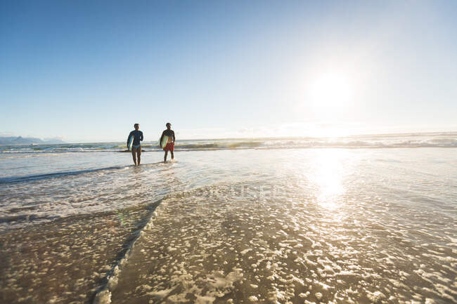 Glückliches afrikanisch-amerikanisches Paar im Meer mit Surfbrettern. gesunde Freizeit im Freien am Meer. — Stockfoto