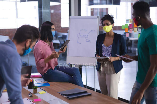 Diverse group of creative colleagues wearing face masks brainstorming in meeting room. independent creative design business during covid 19 coronavirus pandemic. — Stock Photo